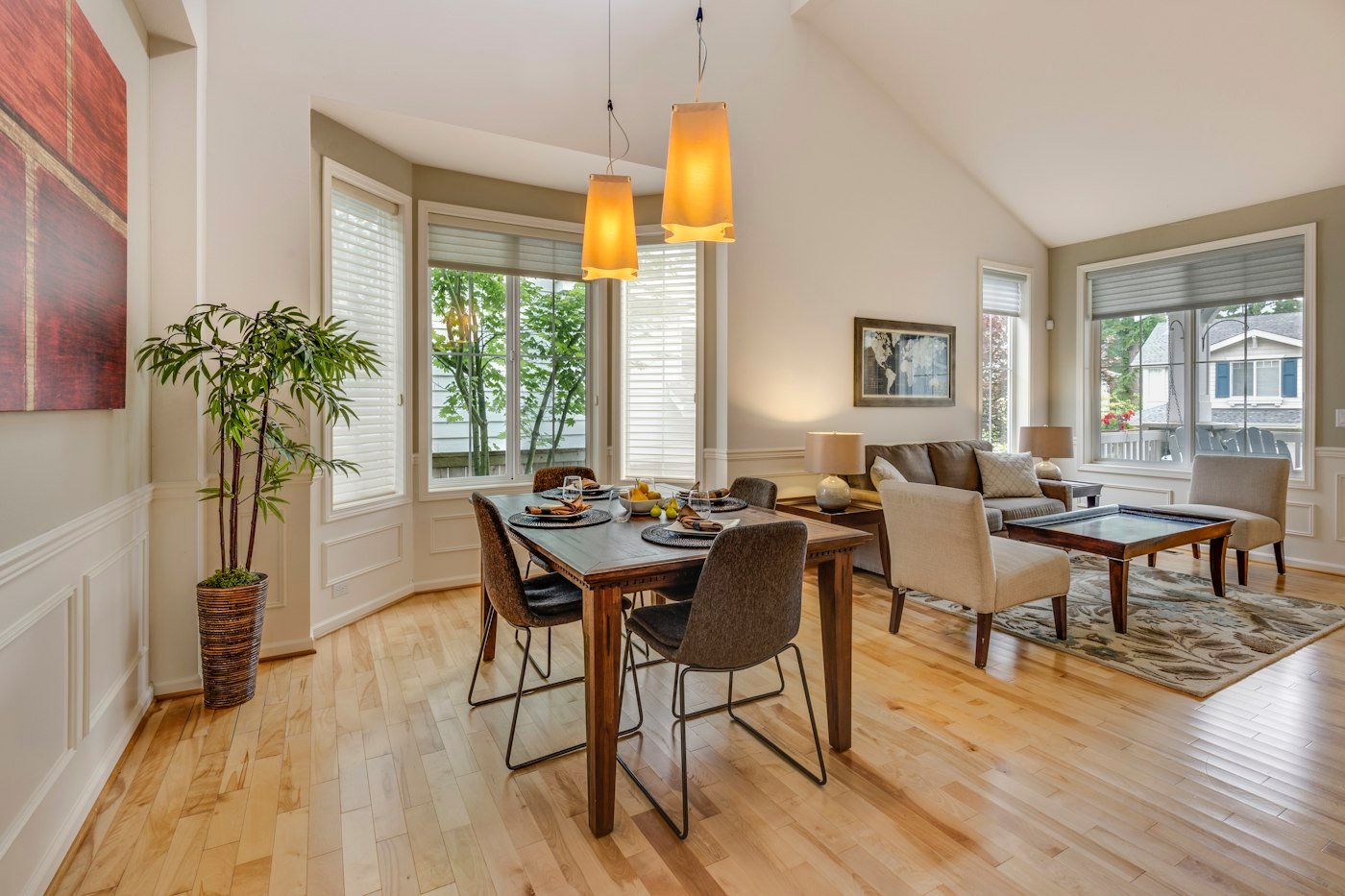 A dining table set for four beside a living area with a sofa, lamps, and two warm pendant lights